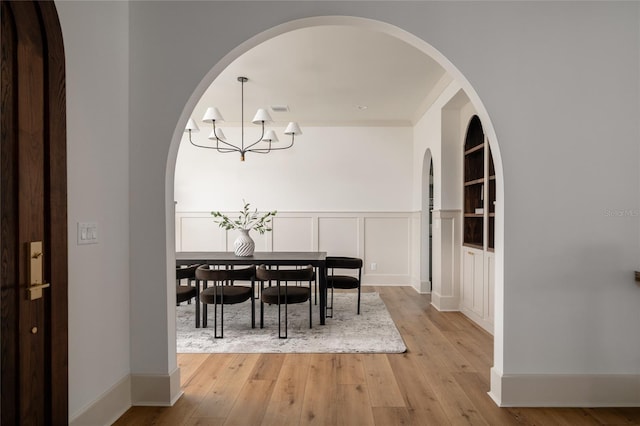 dining room with a wainscoted wall, visible vents, a decorative wall, a chandelier, and light wood-type flooring