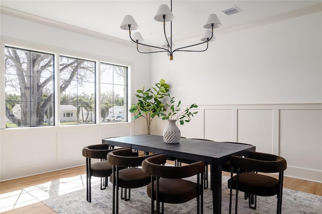 dining space featuring light wood finished floors, visible vents, a decorative wall, and a chandelier