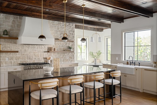 kitchen with tasteful backsplash, wall chimney range hood, white cabinetry, open shelves, and a sink