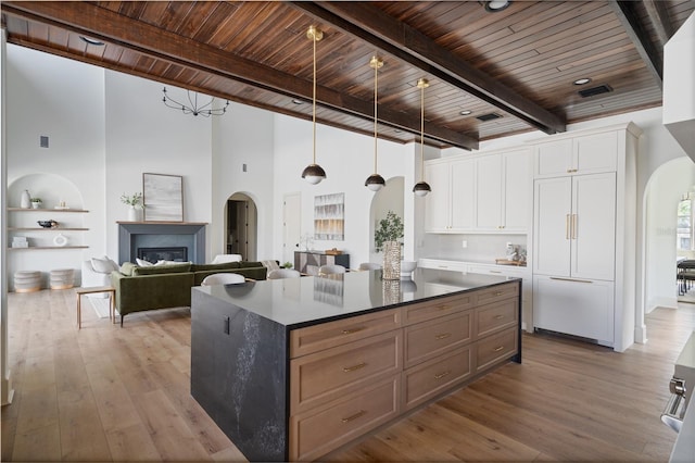 kitchen featuring arched walkways, white cabinets, wooden ceiling, open floor plan, and decorative light fixtures