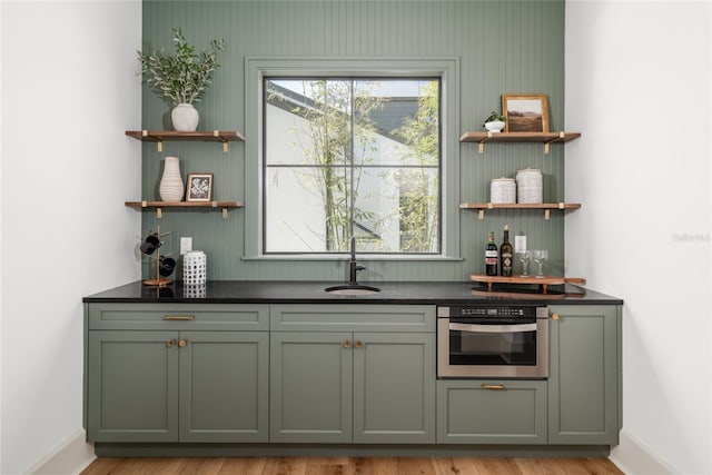 bar with light wood-type flooring, a sink, oven, and baseboards