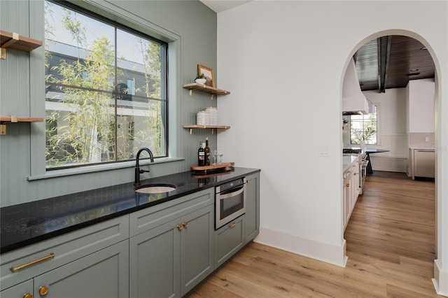 kitchen with light wood finished floors, open shelves, a sink, and oven