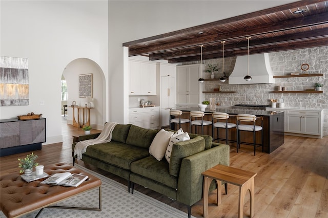 living room with arched walkways, wooden ceiling, beam ceiling, and light wood-style floors