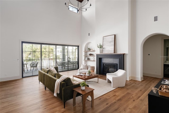 living room featuring light wood-style floors, baseboards, arched walkways, and a tiled fireplace