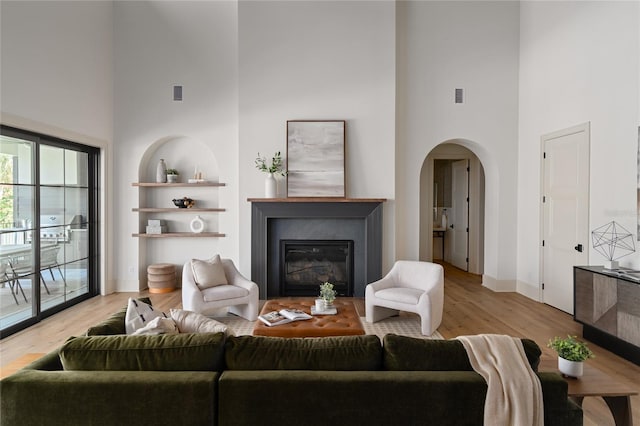 living room featuring light wood finished floors, visible vents, arched walkways, baseboards, and a glass covered fireplace