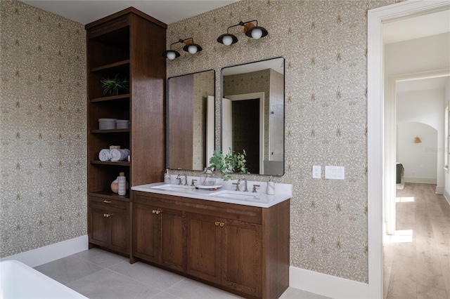 full bathroom featuring double vanity, a sink, baseboards, and wallpapered walls