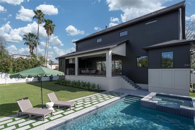 rear view of property with a pool with connected hot tub, a patio area, a lawn, and stairway