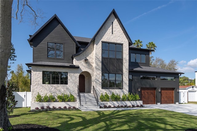 view of front of property featuring an attached garage, fence, driveway, stone siding, and a front yard