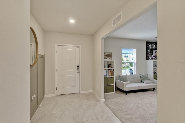 foyer entrance featuring light tile patterned floors, baseboards, visible vents, and light colored carpet