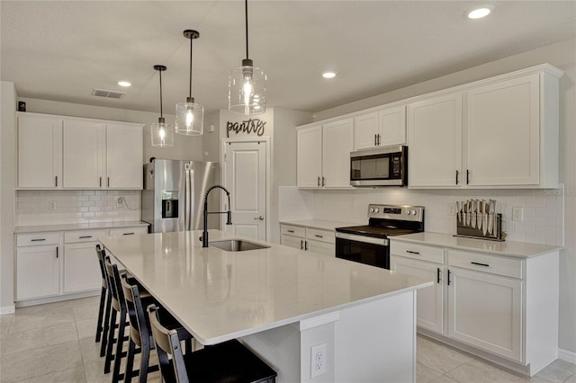 kitchen featuring stainless steel appliances, visible vents, a sink, an island with sink, and a kitchen breakfast bar