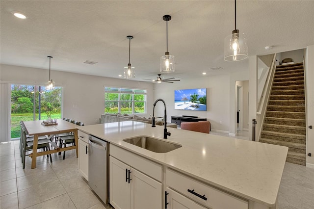 kitchen featuring pendant lighting, open floor plan, white cabinets, a sink, and dishwasher