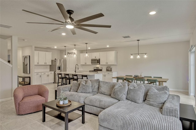 living area with ceiling fan with notable chandelier, baseboards, visible vents, and recessed lighting