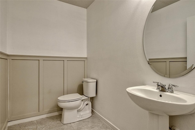 bathroom featuring wainscoting, a sink, toilet, and a decorative wall