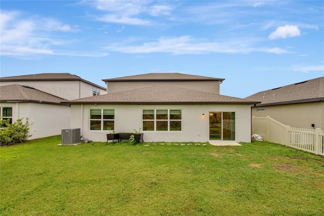 back of property with a yard, a shingled roof, central AC, and fence