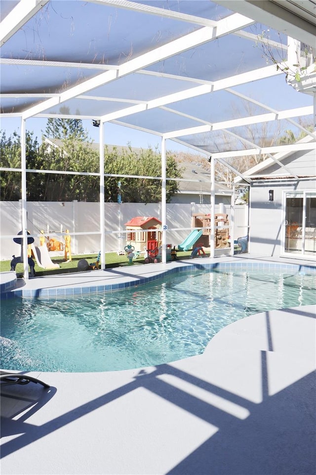 view of pool featuring a patio area, glass enclosure, a playground, and a fenced in pool