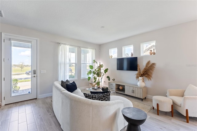 living room featuring visible vents, light wood-style flooring, baseboards, and a textured ceiling