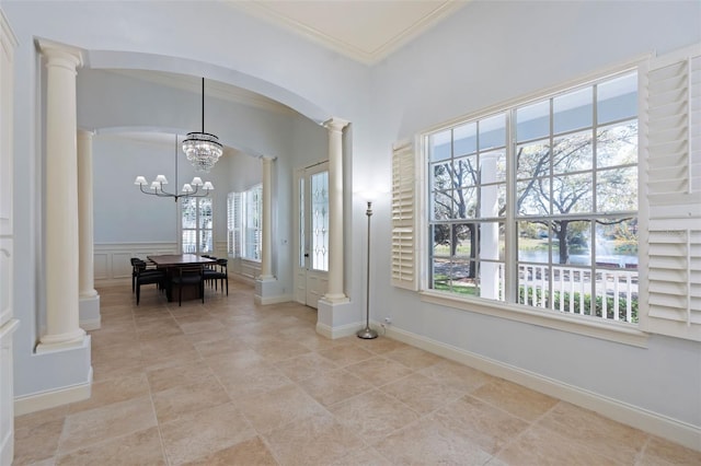 foyer entrance with a decorative wall, a wainscoted wall, ornamental molding, decorative columns, and an inviting chandelier