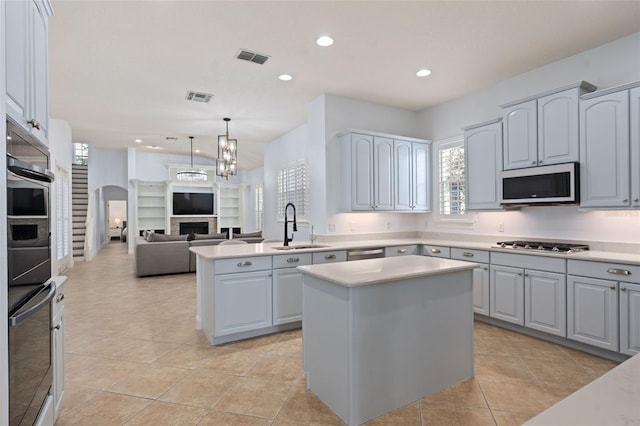 kitchen with stainless steel appliances, a fireplace, a kitchen island, a sink, and visible vents