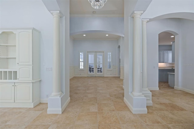 entryway featuring crown molding, arched walkways, decorative columns, and a decorative wall