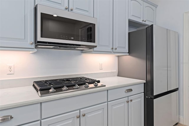 kitchen with stainless steel gas cooktop, light countertops, white microwave, freestanding refrigerator, and white cabinetry