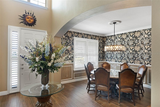 dining room featuring arched walkways, dark wood-style flooring, a wainscoted wall, and a healthy amount of sunlight