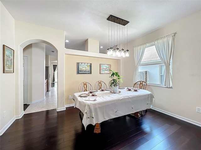 dining area with arched walkways, baseboards, and wood-type flooring