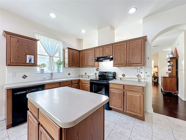 kitchen with backsplash, under cabinet range hood, light countertops, black appliances, and a sink