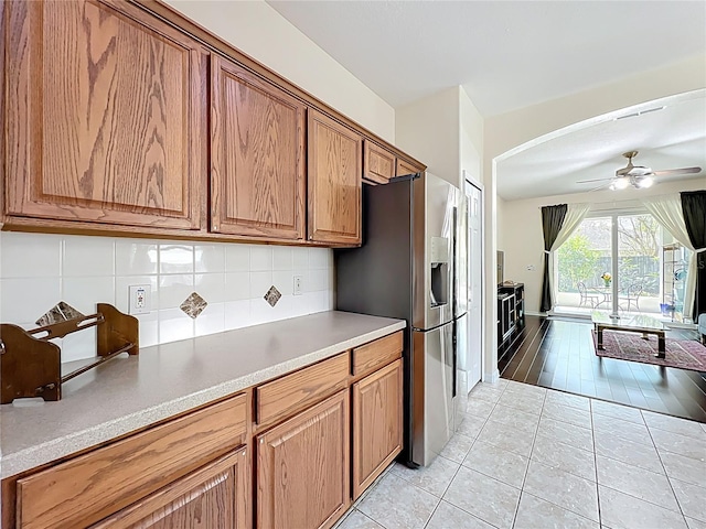 kitchen with tasteful backsplash, brown cabinetry, stainless steel fridge with ice dispenser, light tile patterned flooring, and a ceiling fan