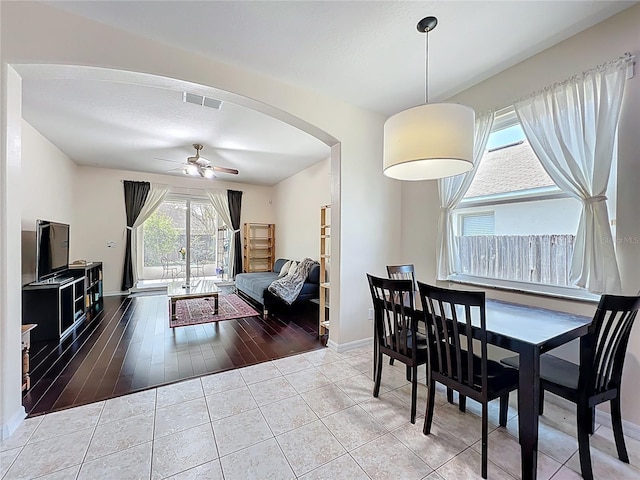 dining space with tile patterned flooring, a ceiling fan, arched walkways, and baseboards