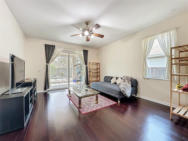 living room featuring a textured ceiling, baseboards, dark wood-type flooring, and ceiling fan