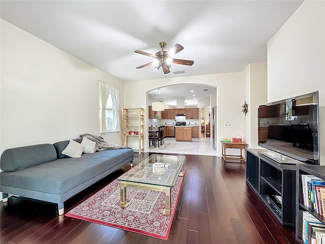 living room featuring a ceiling fan, visible vents, light wood-style floors, and arched walkways