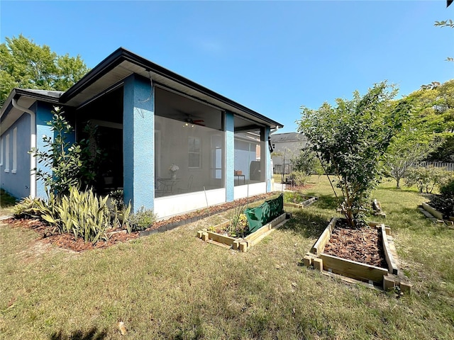 view of side of home featuring a garden, stucco siding, a lawn, and a sunroom