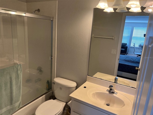 ensuite bathroom featuring a textured wall, toilet, ensuite bathroom, combined bath / shower with glass door, and vanity