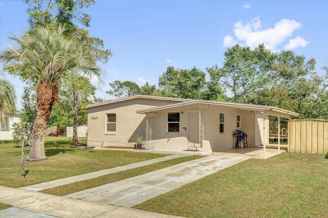 back of property with concrete driveway, stucco siding, fence, and a lawn