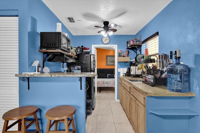 kitchen featuring light tile patterned flooring, visible vents, light countertops, light brown cabinetry, and a kitchen bar