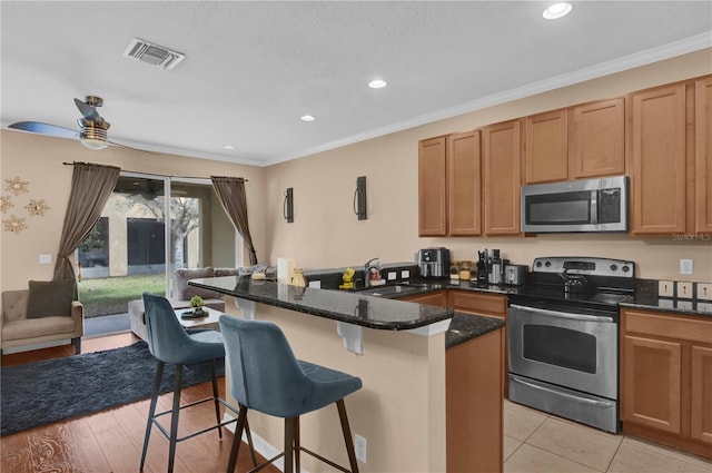 kitchen featuring visible vents, a breakfast bar, a peninsula, stainless steel appliances, and a sink