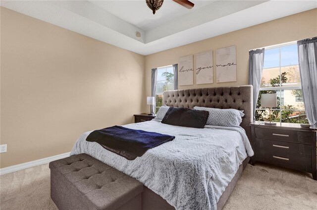 bedroom featuring baseboards, a raised ceiling, a ceiling fan, and light colored carpet