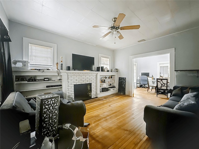 living area with visible vents, a ceiling fan, hardwood / wood-style flooring, and a fireplace