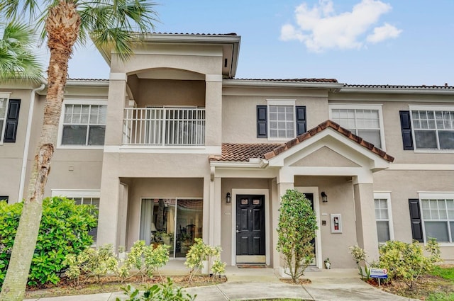 townhome / multi-family property with a tile roof, a balcony, and stucco siding