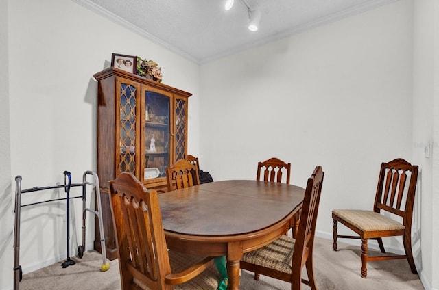 dining space featuring rail lighting, light colored carpet, ornamental molding, a textured ceiling, and baseboards