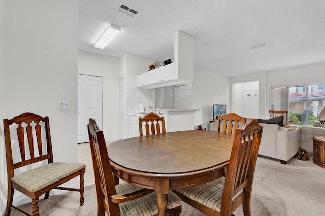 dining room with light carpet, visible vents, and a textured ceiling