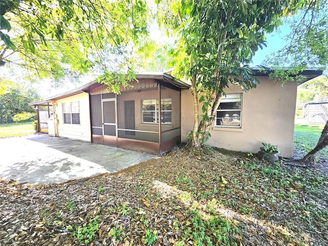 rear view of property with a patio area, a sunroom, and stucco siding