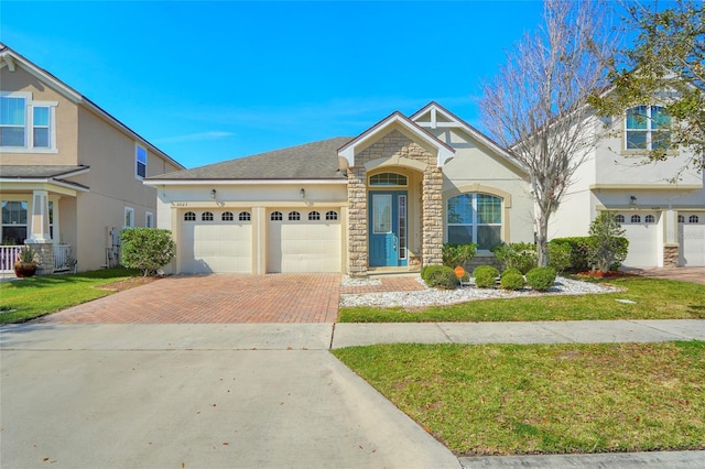 view of front facade featuring stone siding, roof with shingles, decorative driveway, a front lawn, and stucco siding