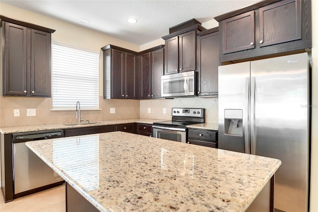 kitchen with appliances with stainless steel finishes, a sink, backsplash, and dark brown cabinets