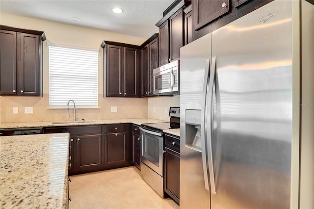 kitchen with light tile patterned floors, dark brown cabinetry, stainless steel appliances, a sink, and decorative backsplash