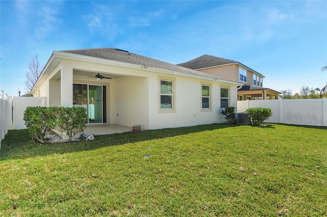 back of property with ceiling fan, a fenced backyard, central AC, a yard, and stucco siding