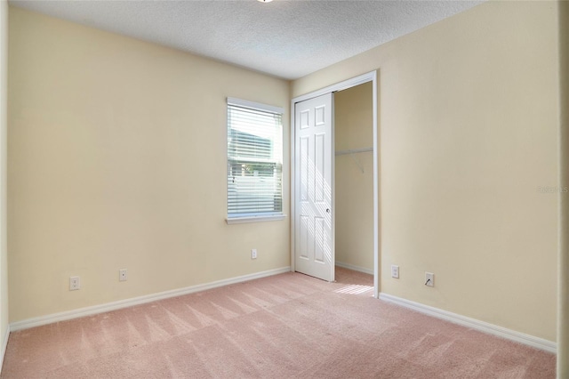 unfurnished bedroom with a closet, light carpet, a textured ceiling, and baseboards