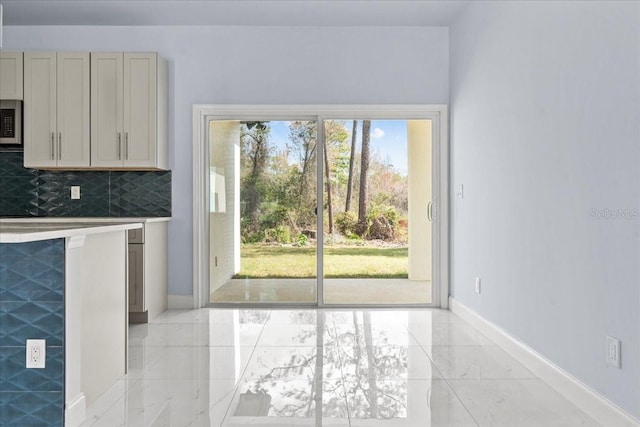 kitchen with marble finish floor, light countertops, stainless steel microwave, backsplash, and baseboards