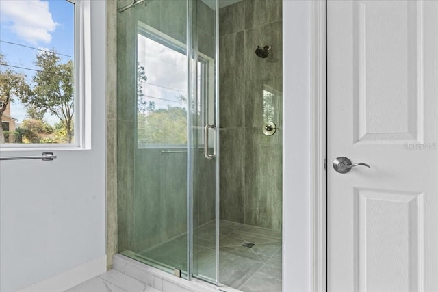 bathroom with marble finish floor, a shower stall, and baseboards