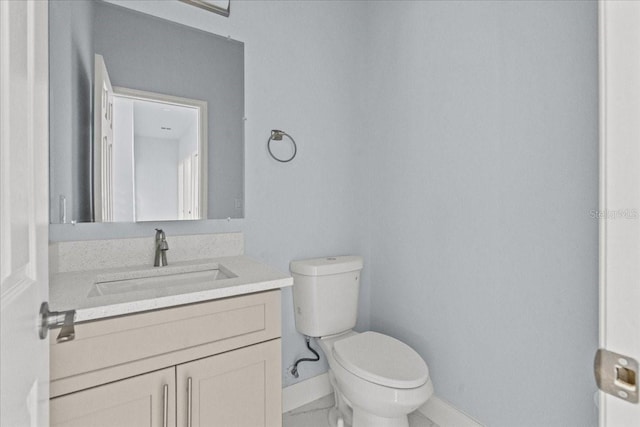 half bathroom featuring toilet, marble finish floor, baseboards, and vanity